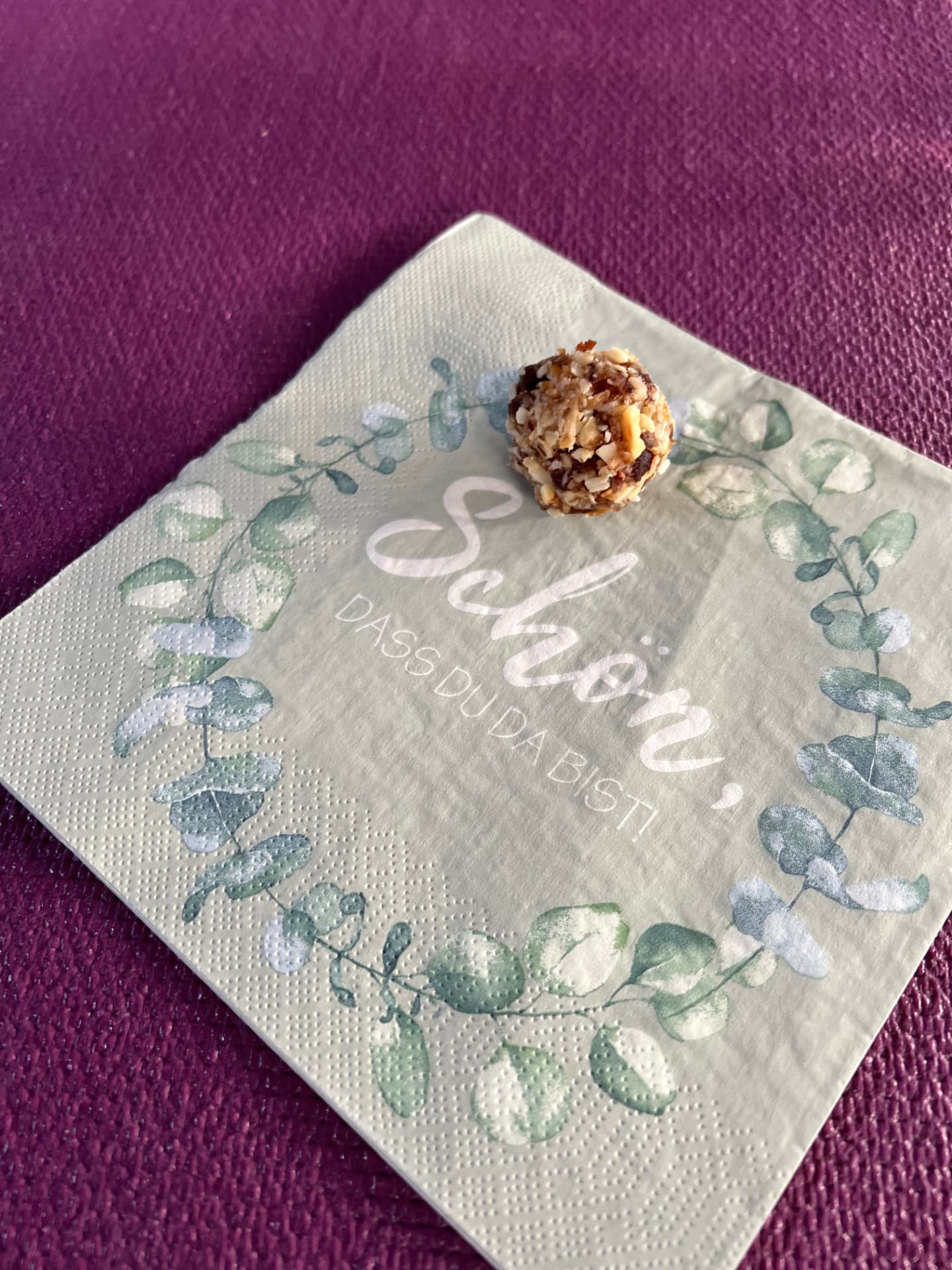 Serviette mit der Aufschrift „Schön, dass du da bist!“ und einem Energiebällchen auf der Yogamatte